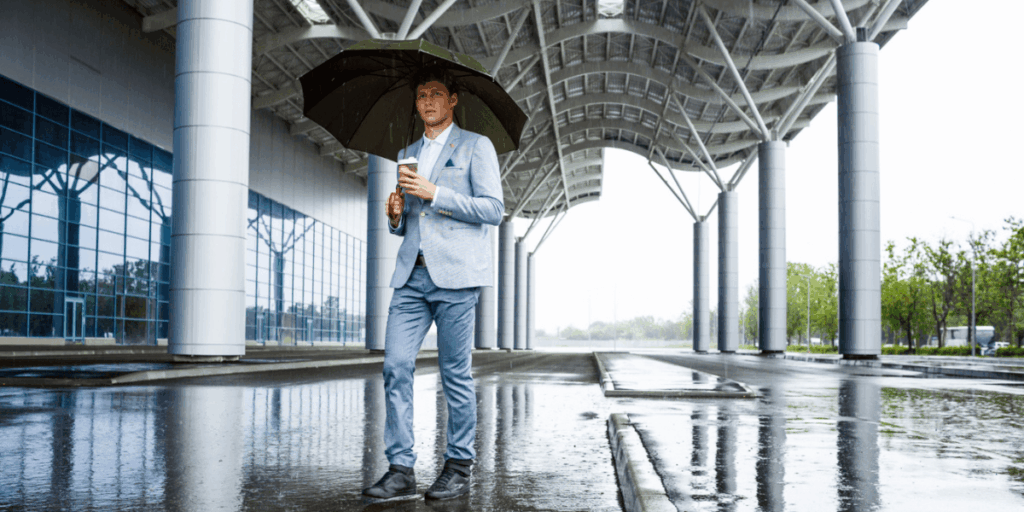A man in a suit stands in the rain, holding an umbrella to shield himself from the downpour.