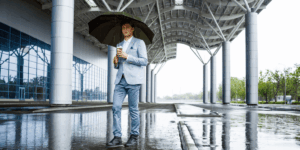 A man in a suit stands in the rain, holding an umbrella to shield himself from the downpour.